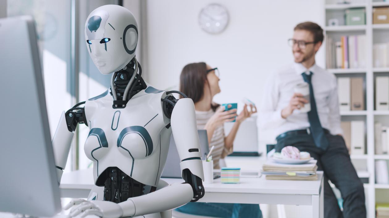 Un robot stă la un birou, în fața unui calculator și muncește. În spatele lui sunt un bărbat și o femeie, care discută între ei, sunt fericiți și beau o cafea. Bărbatul să pe biroul femeii și este îmbrpcat cu o cămașă albă, pantaloni eleganti gri și o cravată albastră la gât. Femeia stă pe un scaun, în spatele biroului său, poartă o bluză albă cu dungi negre. Amândoi poartă ochelari și țin în mână câte o ceașcă de cafea.