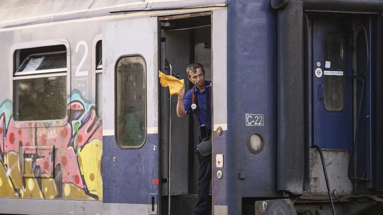 Un angajat CFR semnalizeaza intrarea unui tren in gara cu un steag galben în mână