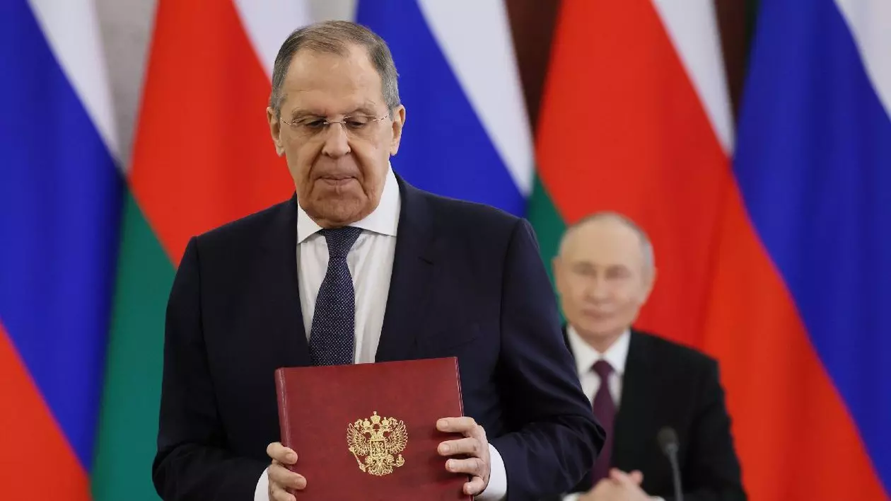 Serghei Lavrov, îmbrăcat în costum negru, cămașă albă și cravată neagră, tine în mână o mapă grena, cu o stemă argintie. În fundal se vede Vloadimir Putin Foto: Hepta