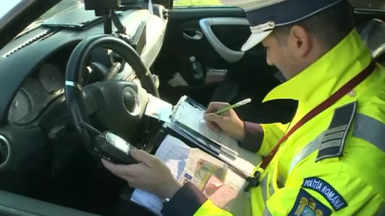 Un polițist cu uniformă este în mașină și scrie o amendă pentru un șofer, iar lângă el are niște bancnote