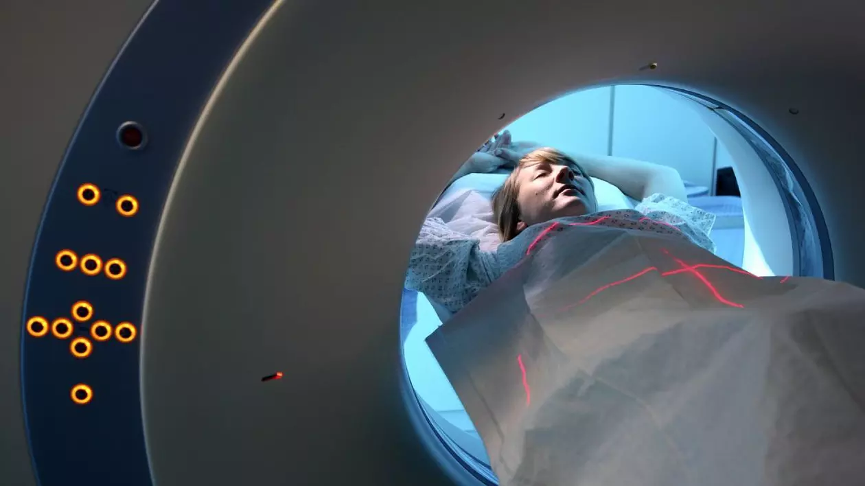 persoană în halat medical întinsă într-un aparat cu radiatii care efectuează o scanare CT