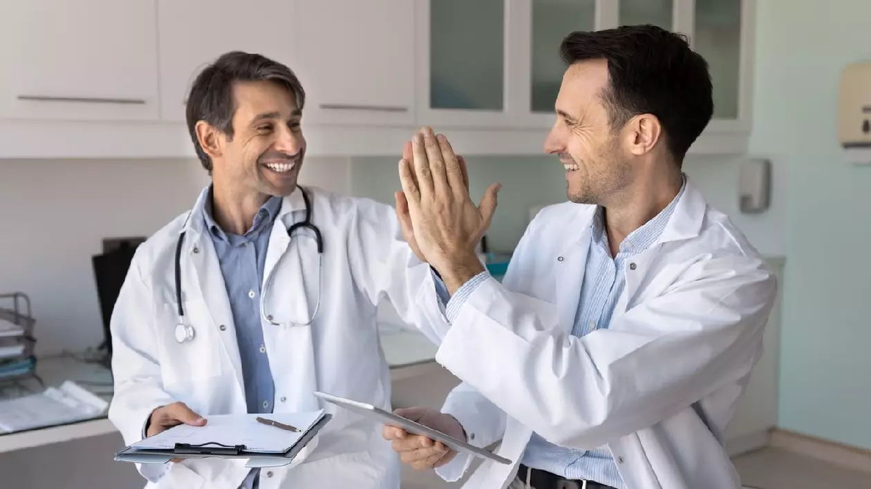 Doi colegi de vârstă mijlocie, lucrători medicali prietenoși, au bătut palma, s-au întâlnit în sala de consultații modernă cu tabletă și clipboard. Lucru în echipă eficient, pozitiv, recunoaștere reciprocă pentru lucrul bine făcut împreună