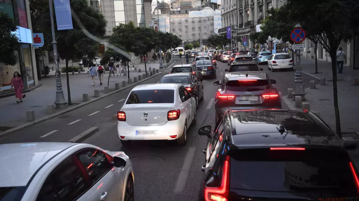 Trafic intens pe Calea Victoriei din centrul Bucureștiului. Se pot observa mai multe mașini în mișcare lentă. Pe partea stângă a imaginii se află trotuarul cu trecători, stâlpi ornamentali și indicatoare rutiere.
