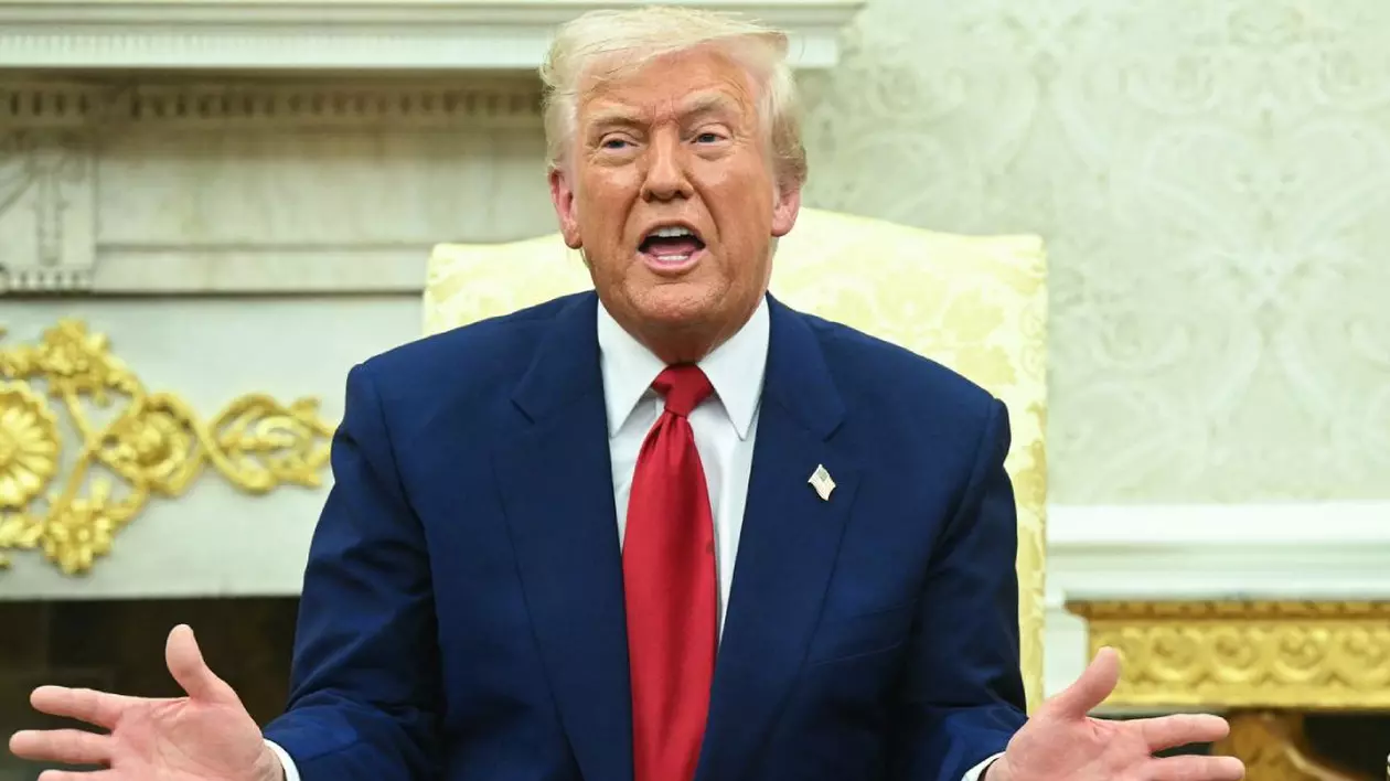 Președintele SUA, Donald Trump, în timpul unui discurs ținut la Casa Albă. Este îmbrăcat într-un sacou bleumarin, cămașă albă și o cravată roșie, în timp ce stă pe un scaun, gesticulează și vorbește