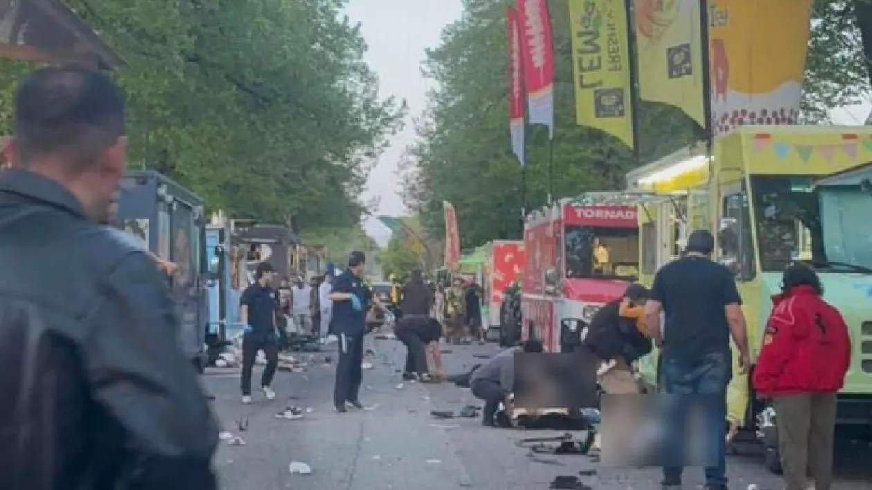 Oameni în picioare pe o stradă și alții întinși pe jos, polițiști care supraveghează zona și autobuze colorate pe partea dreaptă