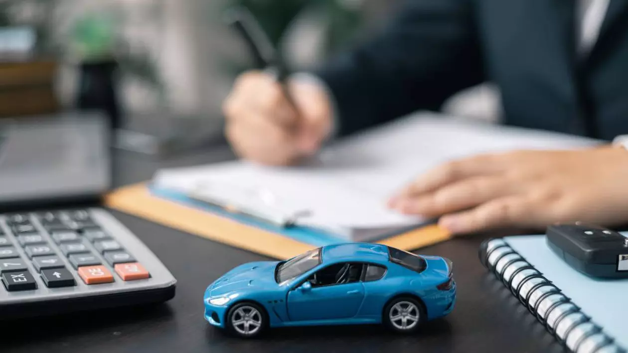 imagine în care în prim-plan, se află o mașină miniaturală albastră, Alături se observă o cheie auto și un caiet de notițe