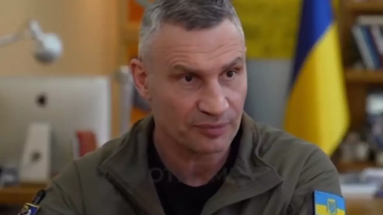 În imagine este ilustrat un bărbat care poartă un tricou negru. De asemenea, pe mâneca hainei sale de culoare verde kaki se poate vedea un ecuson cu steagul Ucrainei