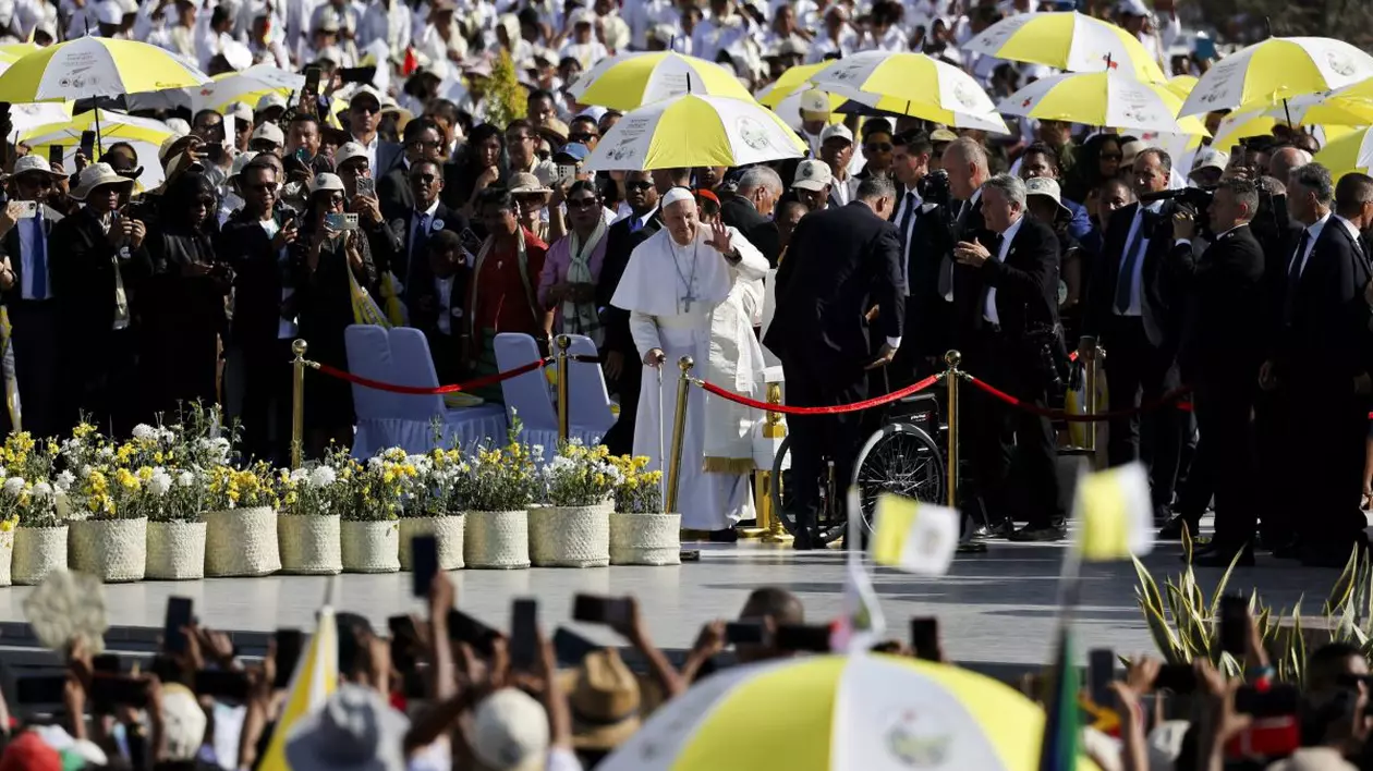 Papa Francisc în mijlocul imaginii, în timpul vizitei sale în Timorul de Est, ținând o umbrelă în culorile naționale ale statului asiatic.