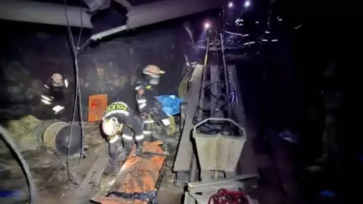 Imagini intunecate din interiorul unei mine cu doi asalvatori, unul in picioare si unul aplecat, mai multi scripeti in jur si lumina de la lanterne