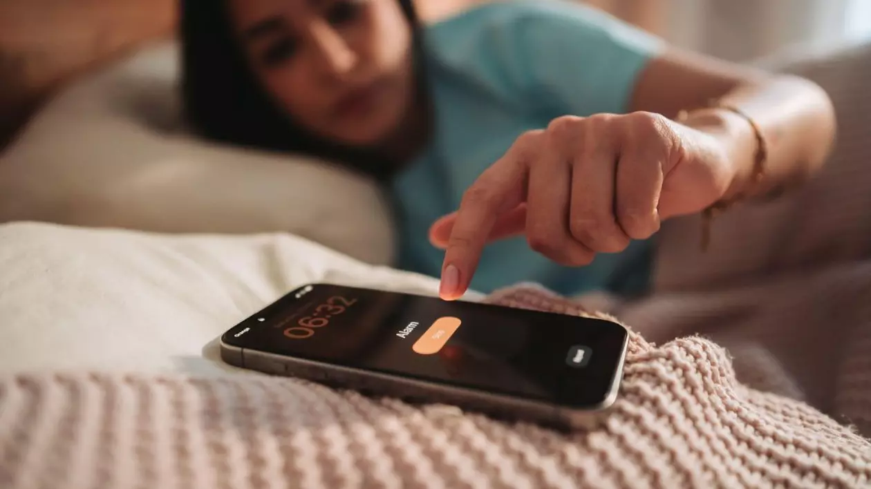 O vedere de aproape a unei persoane care își oprește alarma de dimineață pe un smartphone în timp ce este în pat
