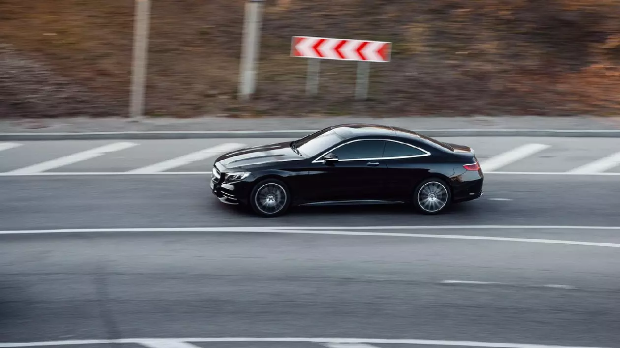 Mercedes coupe negru conducând pe un drum. Profil lateral vedere aeriană a elegant E-class coupe în mișcare la apus de soare.