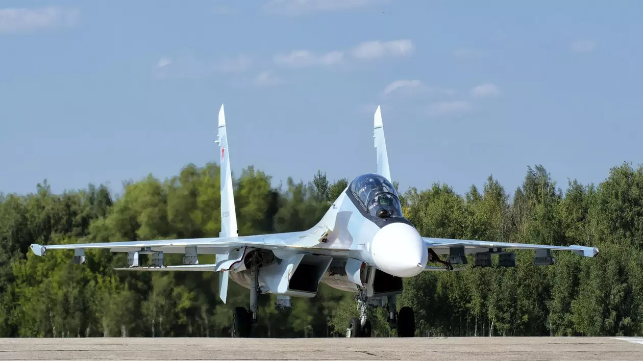 avion de vânătoare rus Suhoi Su-30, de culoare albastru-alb, se pregateste sa aterizeze pe un aerodrom inconjurat de o padure