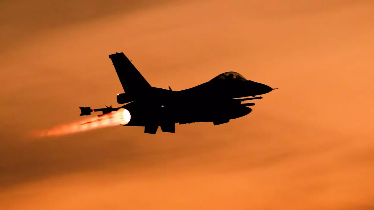 Avion de vânătoare F-16, în umbră, în timp ce decolează, pe un cer colorat în roșu de apusul Soarelui