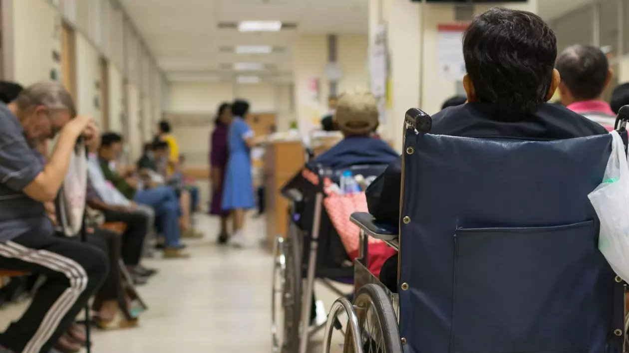 Pacient în vârstă în scaun cu rotile și mulți pacienți care așteaptă un medic și o asistentă medicală în spital