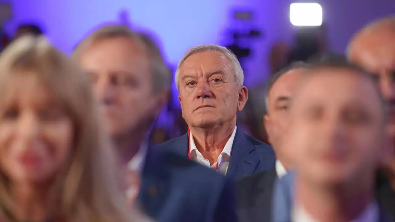 Primarul Buzăului, Constantin Toma la ședința PSD, îmbrăcat la costum, este fotografiat în timp ce stă pe scaun în sală.