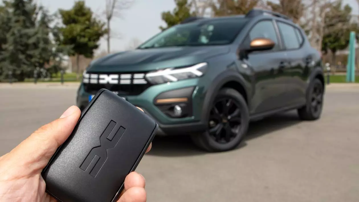 Persoană care ține în mână o cheie a unei mașini model Dacia Sandero. Pe fundal se află un model auto Dacia Sandero Stepway de culoare verde închis.