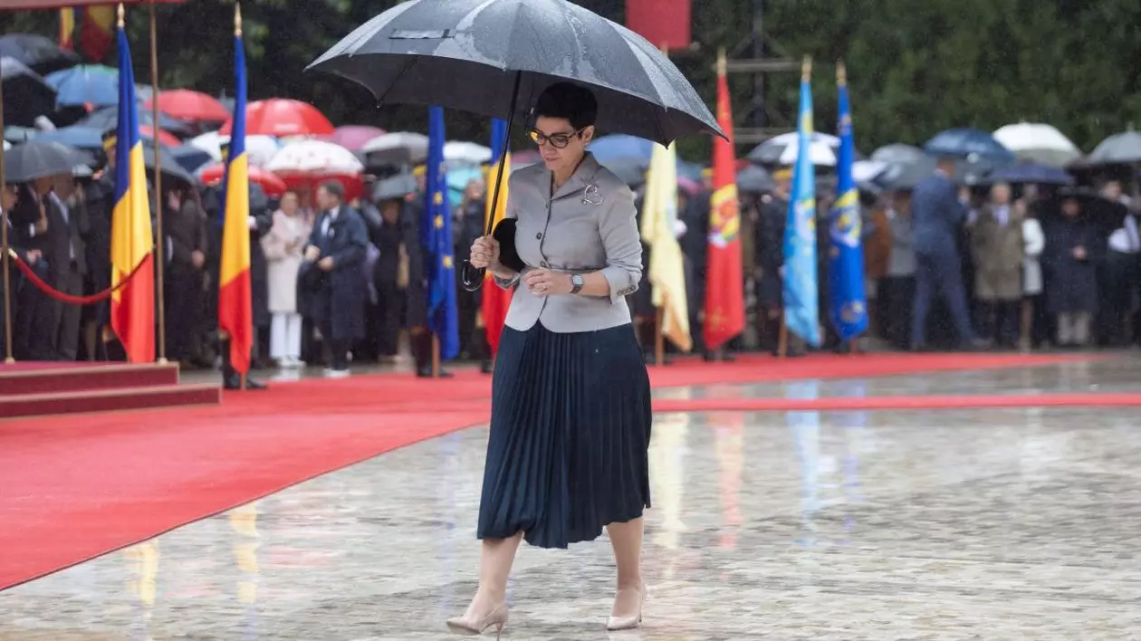 Delia Dinu, cel mai longeviv consilier prezidențial, afară, merge prin ploaie la o ceremonie, ține o umbrelă inchisa la culoare si un plic negru la subrat