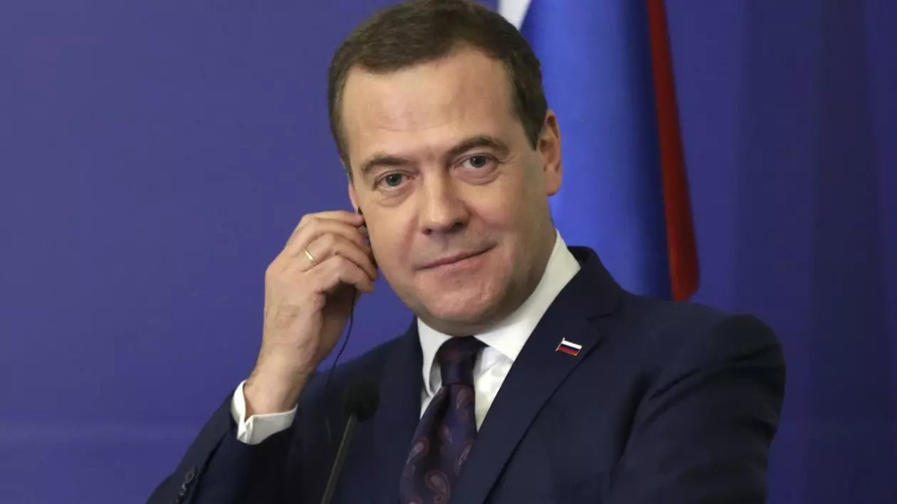 Dmitry Medvedev in costum negru si cravata, cu mana dreaptă la ureche