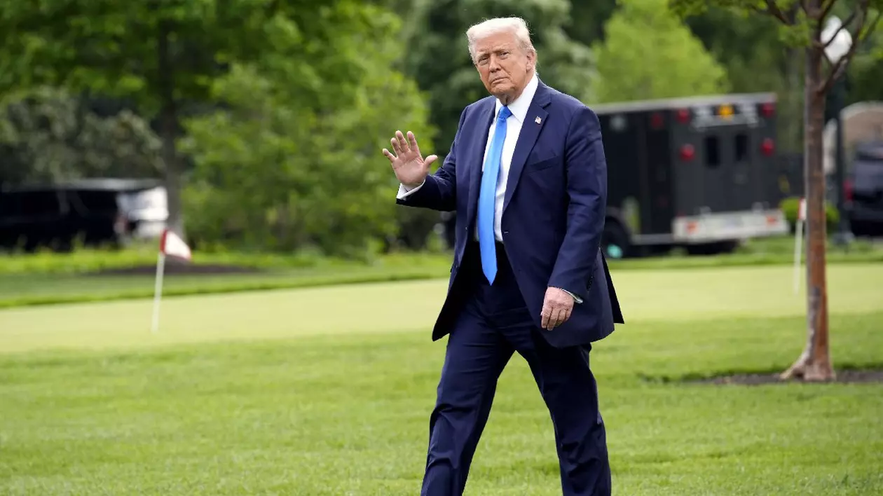 Donald Trump îmbrăcat în costum bleumarin, cămașă albă și cravată bleu, face cu mâna. Președintele american Donald Trump se plimbă pe peluza de sud a Casei Albe din Washington înainte de plecarea sa în Alabama pe 1 mai 2025.