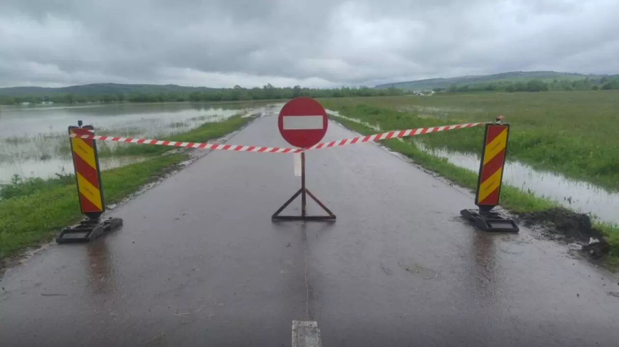 Imaginea surprinde un drum județean complet închis circulației, marcat cu bandă de interdicție și semn de acces interzis, din cauza inundațiilor.