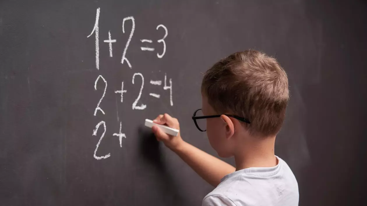 Elev de vârstă mică face calcule la matematică cu creta pe o tablă la școală.