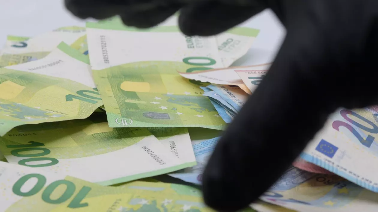 o mână cu o mănușă neagră și multe bancnote de 100 de euro