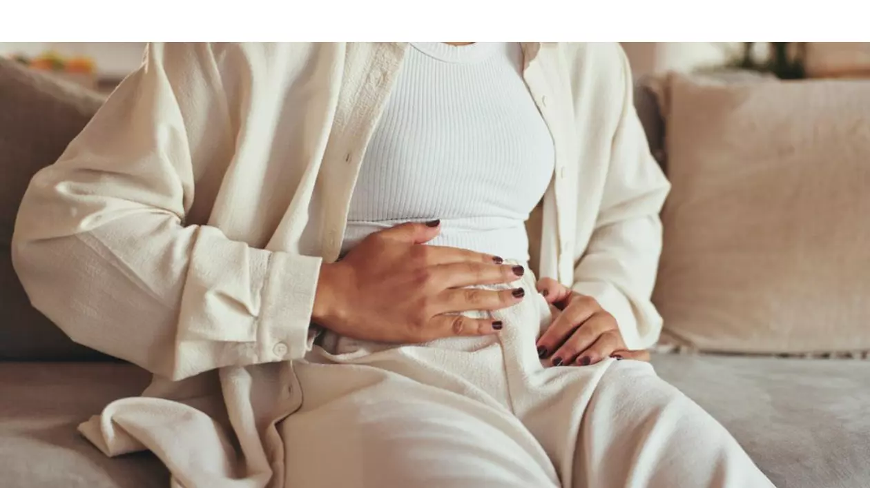 No Spa - femeie imbracata in n=bej, stand pe canapea, tinand mana stanga pe abdomen.