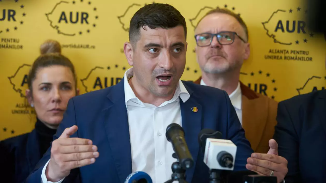 George Simion, îmbrăcat într-un sacou bleumarin și o cămașă albă, la sediul AUR, în timp ce susține o conferință de presă și gesticulează.