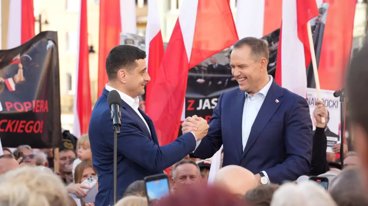 George Simion și Karol Karol Nawrocki dau mână pe o scenă, în timpul unui miting electoral din Polonia, sunt înconjurați de steaguri alb/roșii