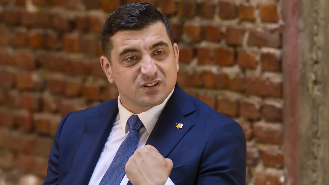 George Simion, îmbrăcat într-un costum de culoare albastră, având în spate un perete de cărămidă