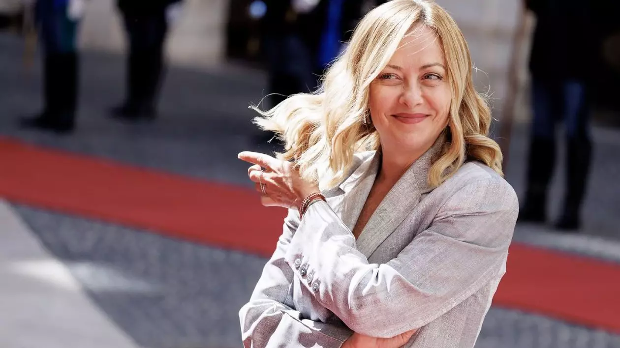 Giorgia Meloni , intr-un costum deschis la culoare, zâmbeste fericita in timp ce isi da cu mana stangă prin par, mana dreapta incrucisată la piept