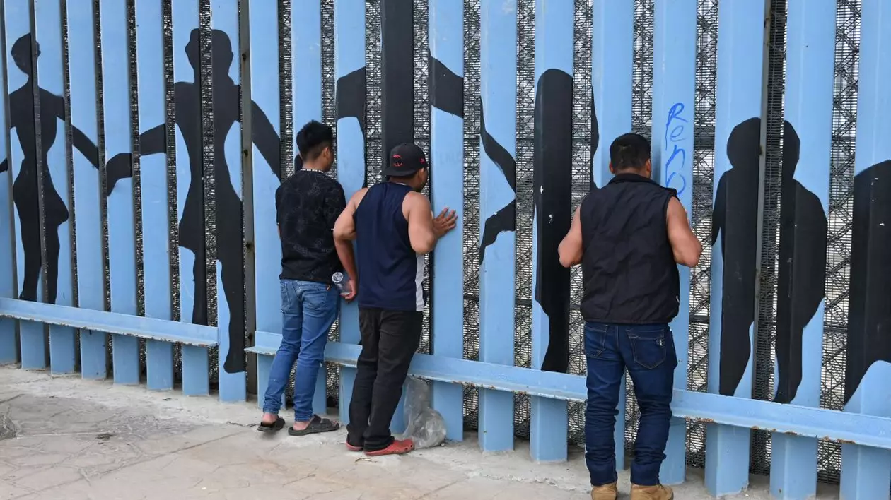 Mai multe persoane privesc prin gardul de frontieră în timp ce trupele Corpului de Marină al Statelor Unite patrulează de-a lungul zonei de graniță a plajei SUA-Mexic, Tijuana-San Diego
