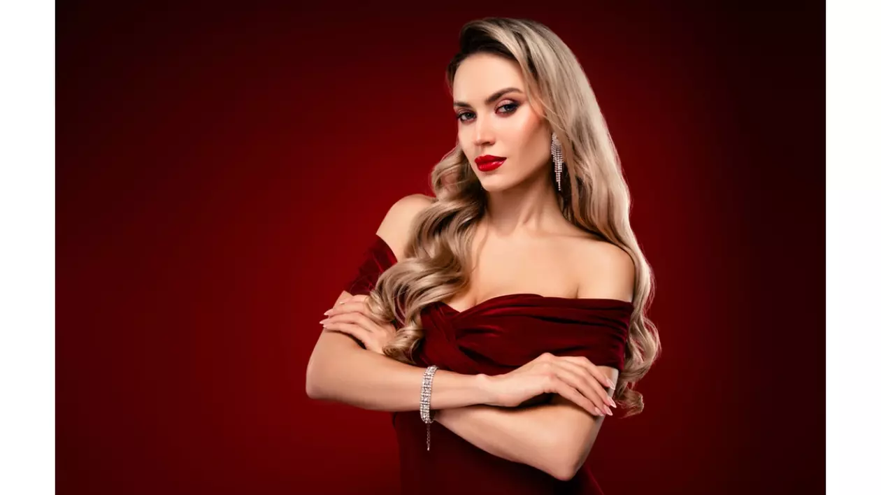 Femeie blonda, atragatoare cu parul lung si ondulat, poarta o rochie eleganta cu umerii goi visinie