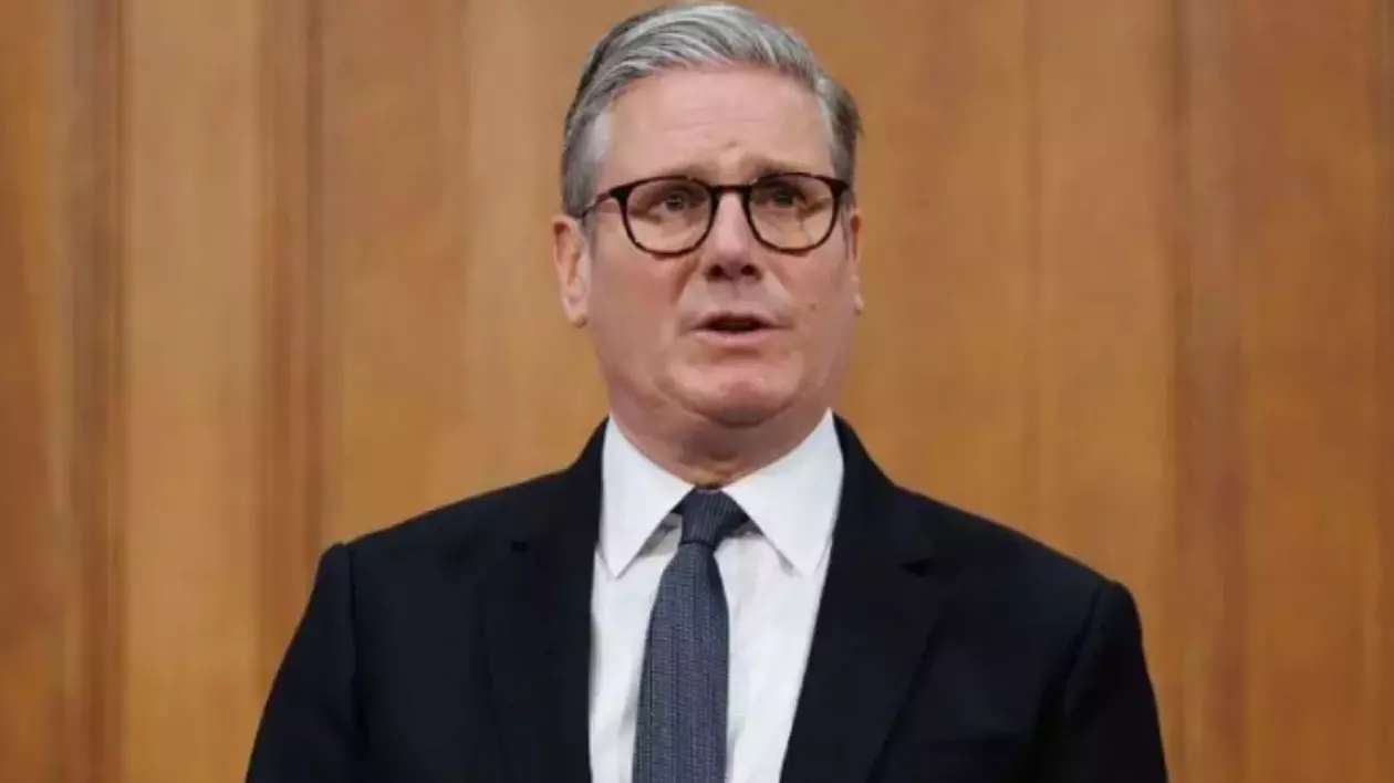În imagine este ilustrat Keir Starmer, un bărbat îmbrăcat în costum negru, cămașă albă și cravată gri.