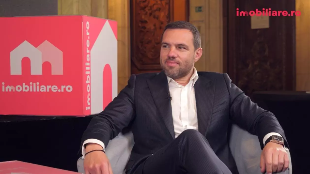 Laurențiu Afrasine, îmbrăcat în costum, în timp ce stă pe scaun, în studioul Imobiliare.ro deschis la Salonul Imobiliar București