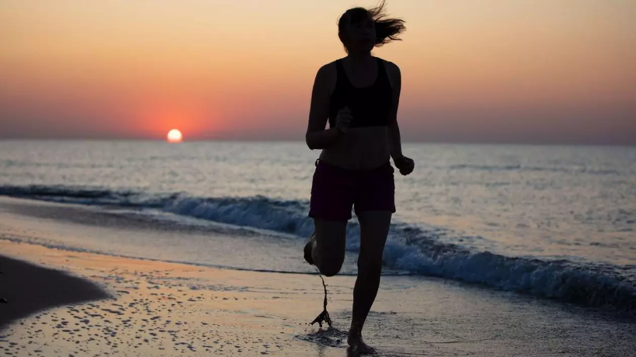 Silueta unei atlete care aleargă pe nisip, pe fundalul răsăritului de soare pe mare