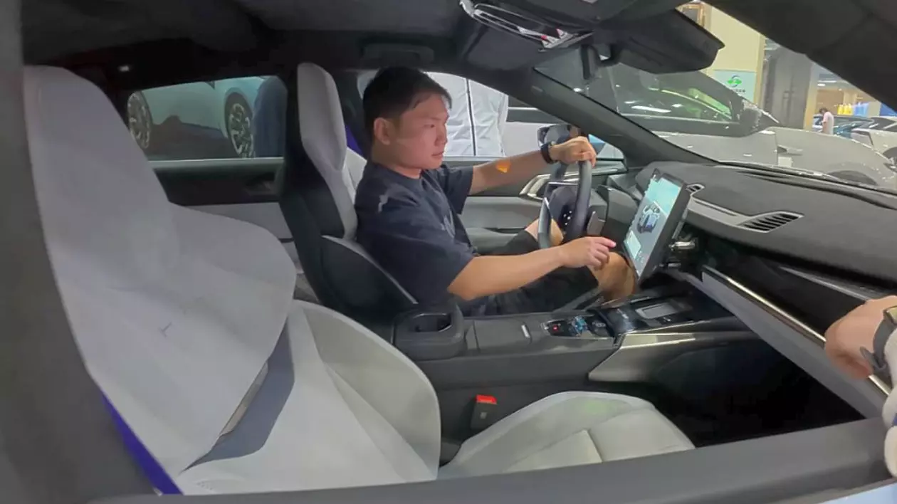 Interiorul unei mașini electrictrice chinezești. În prim-plan, un bărbat se află pe locul șoferului, care testează mai multe functionalități ale mașinii.