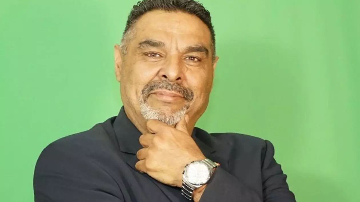 portret bărbat in costum, cu mana stângă la bărbie, la mana un ceas masiv aurit, pe un fundal verde
