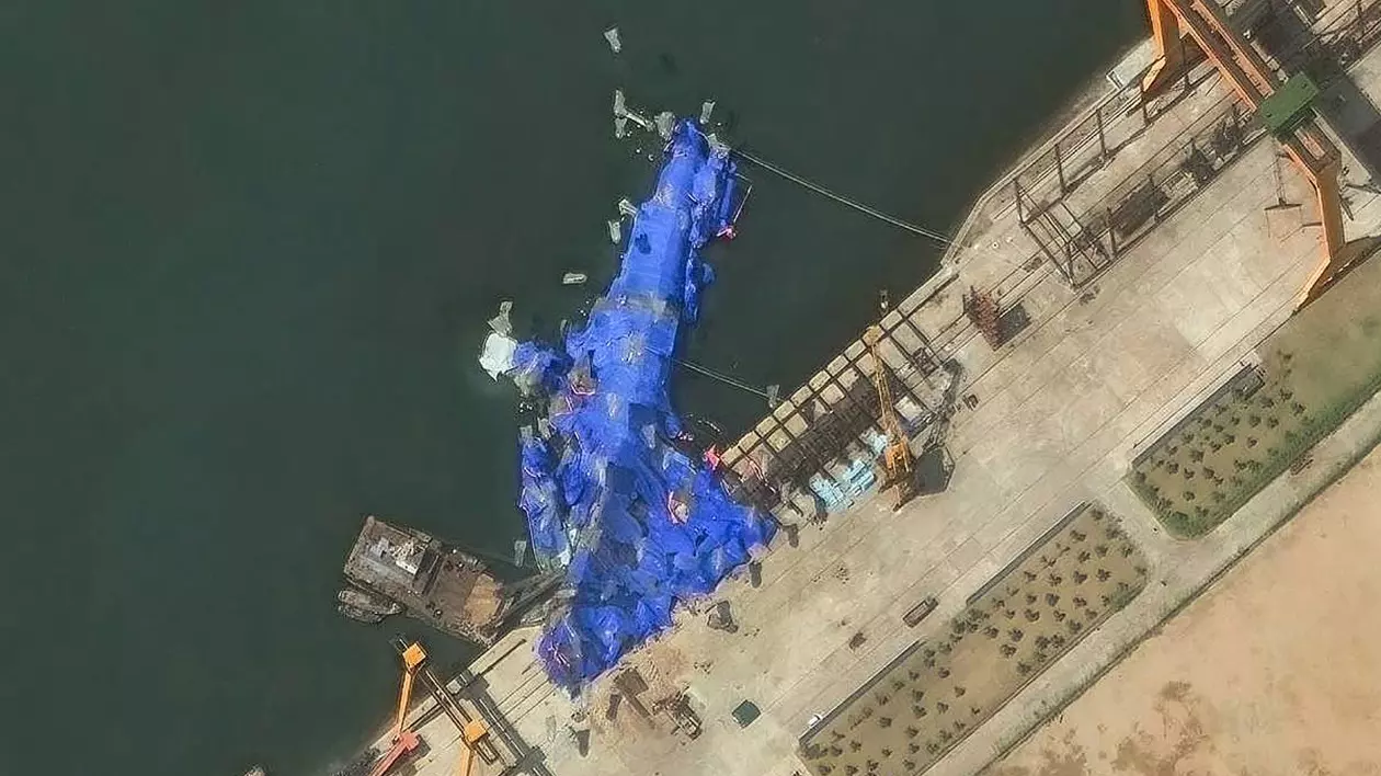 Nava de război este eșuată la mal și acoperită cu o prelaă albastră peste care se văd mai multe obiecte transparente în formă de balon.