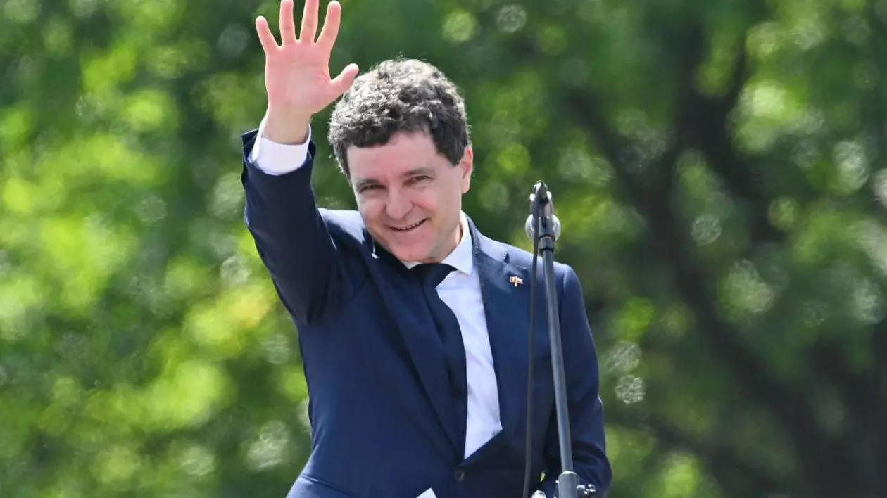 Nicușor Dan îmbrăcat într-un costum albastru, în timpul unui discurs pe care îl ține în aer liber, în dreptul unor copaci cu frunze verzi.
