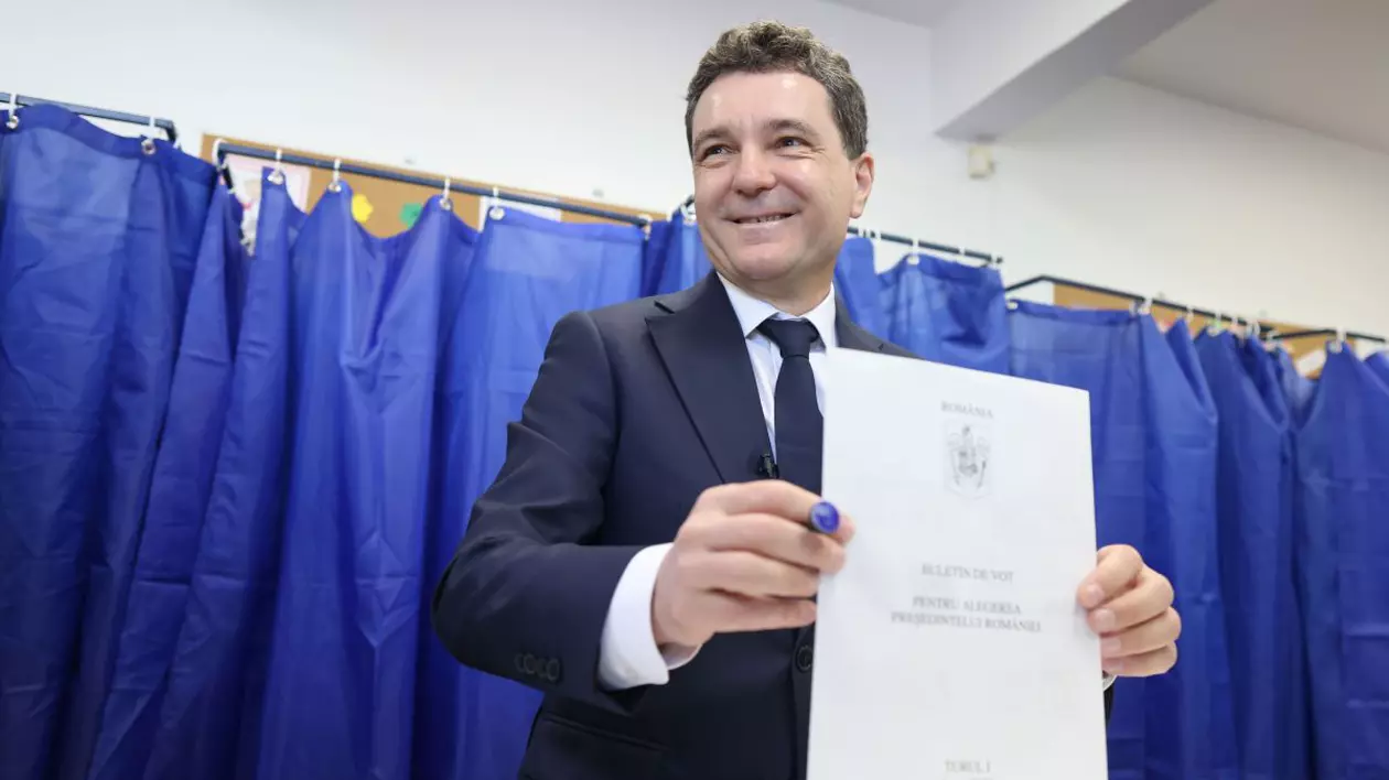 Nicosor Dan în costum inchis la culoare si cămasă albă introduce buletinul de vot in urnaă, in spatele lui perdele albastre de la cabina de vot