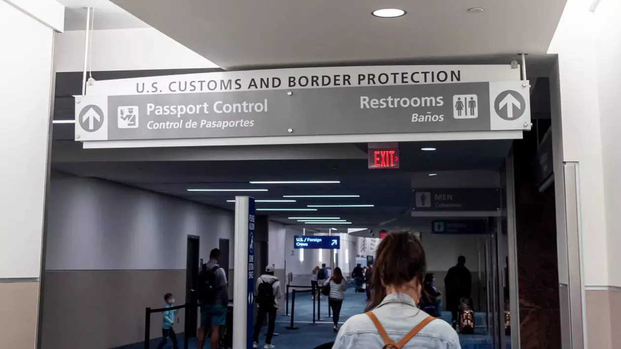 O femeie șatenă cu un ghiozdan în spate stă și așteaptă controlul de la vamă, într-un aeroport, pentru a putea intra în SUA.