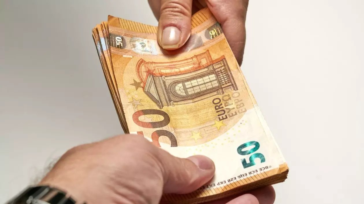 Mâna unui bărbat care ține mai multe bancnote de 50 de euro și le îndreaptă spre o femeie care a pus mâna pe ele