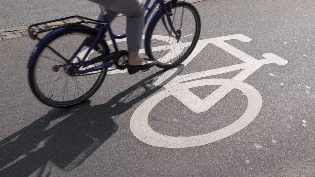 Pista de bicicleta, se vede o parte dintr-o bicicleta pe care merge o femeie imbracata in pantaloni gri și care poarta niste pantofi fara toc, negri