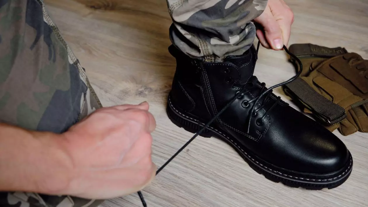 Bărbat în uniformă militară își leagă șireturile la pantofii negri