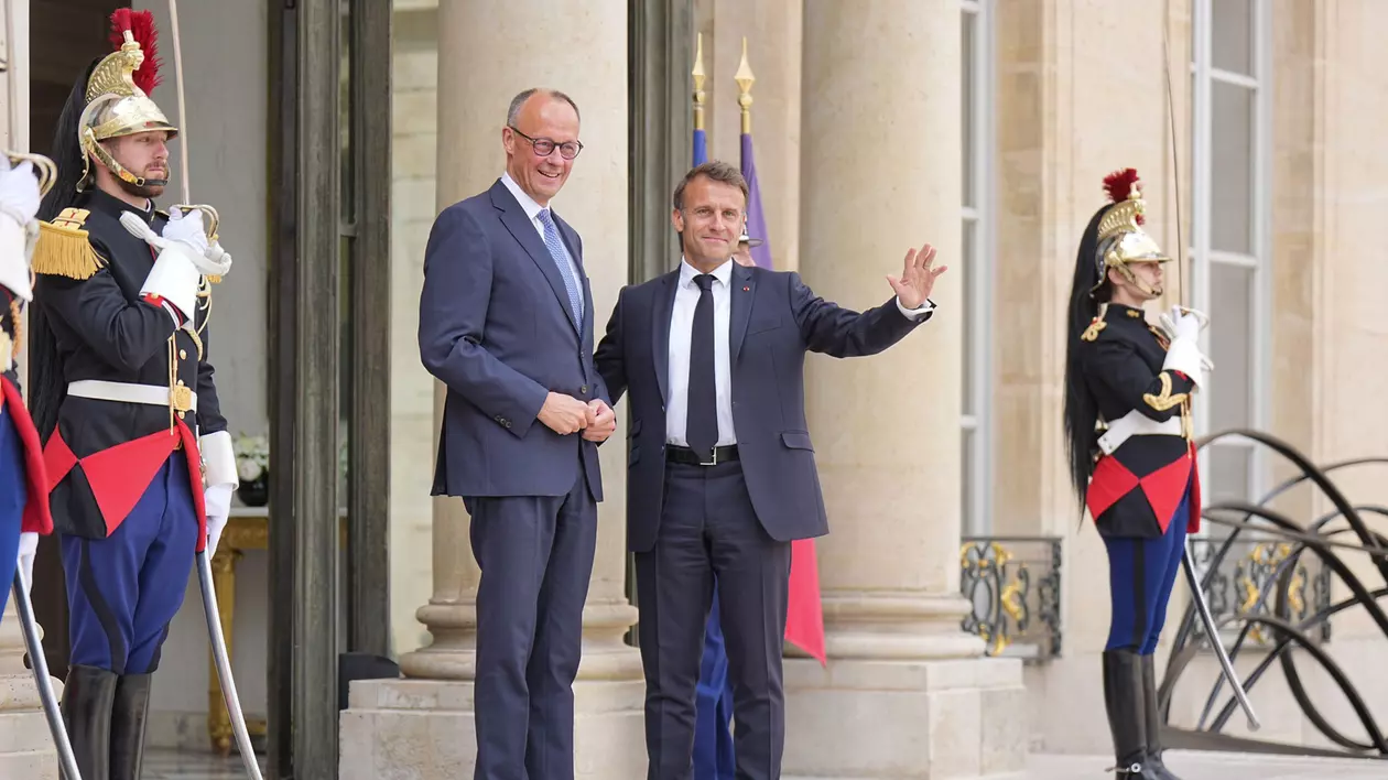 Președintele francez Emmanuel Macron âîl primește pe cancelarul german Friedrich Merz la pris. Cei doi dau mâna ș zîmbesc. Alături se află doi soldați din garda franceză