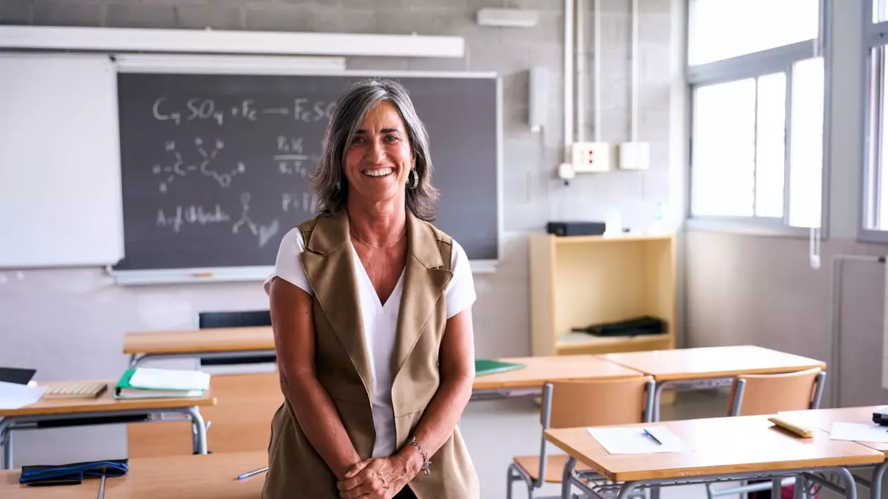 O profesoara sta singura intr-o sala de clasa goala, rezemată de o bancă