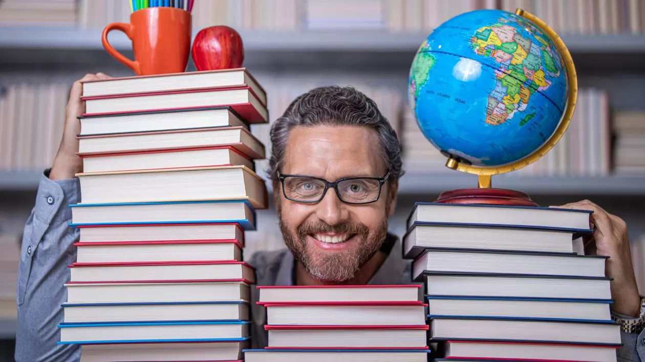 Profesor cu ochelari care zâmbește și ține pe umeri mai multe cărți
