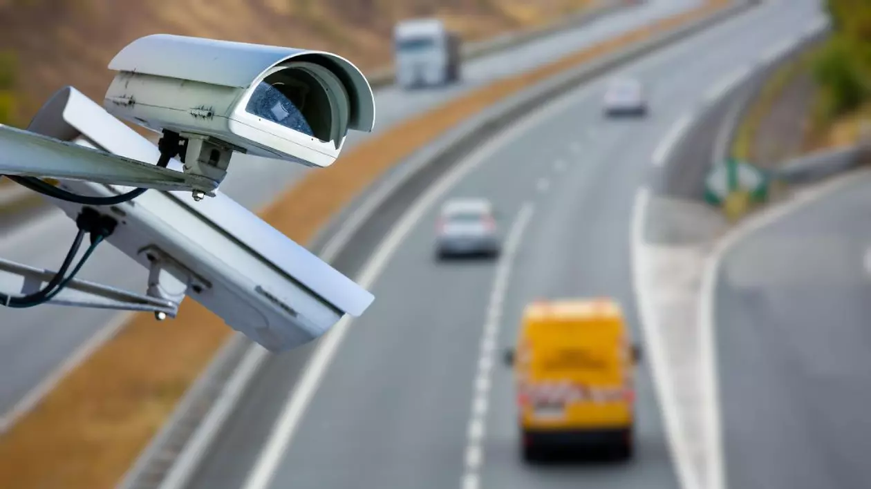Două camere de securitate care supraveghează un drum pe care circulă trei mașini, pe fundal blurat