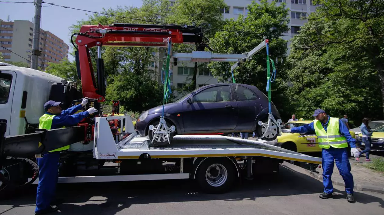 Ridicare a unei mașini parcat ilegal în București. În imagine apar doi angajați îmbrăcați în uniforme reflectorizante